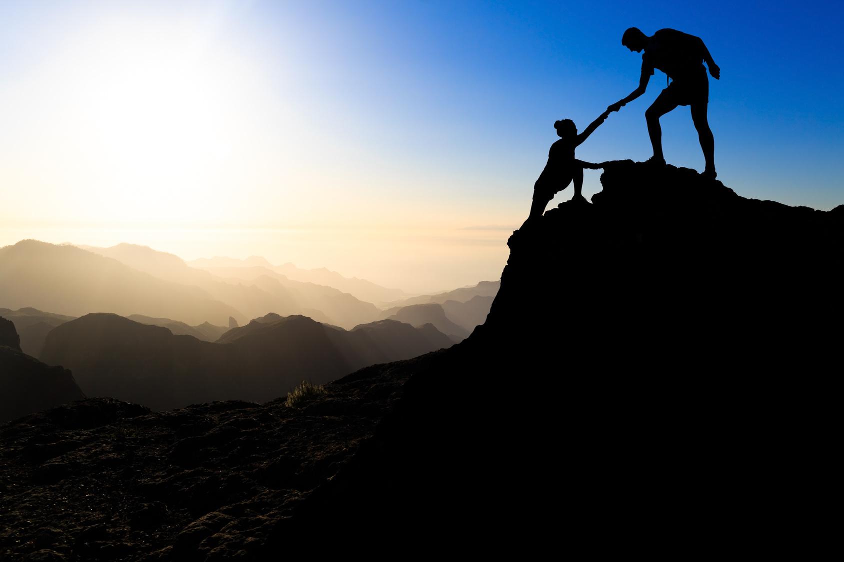 Teamwork couple hiking help each other trust assistance silhouette in mountains, sunset. Team of climbers man and woman hiker helping each other on top of mountain, climbing trust, beautiful sunset landscape.