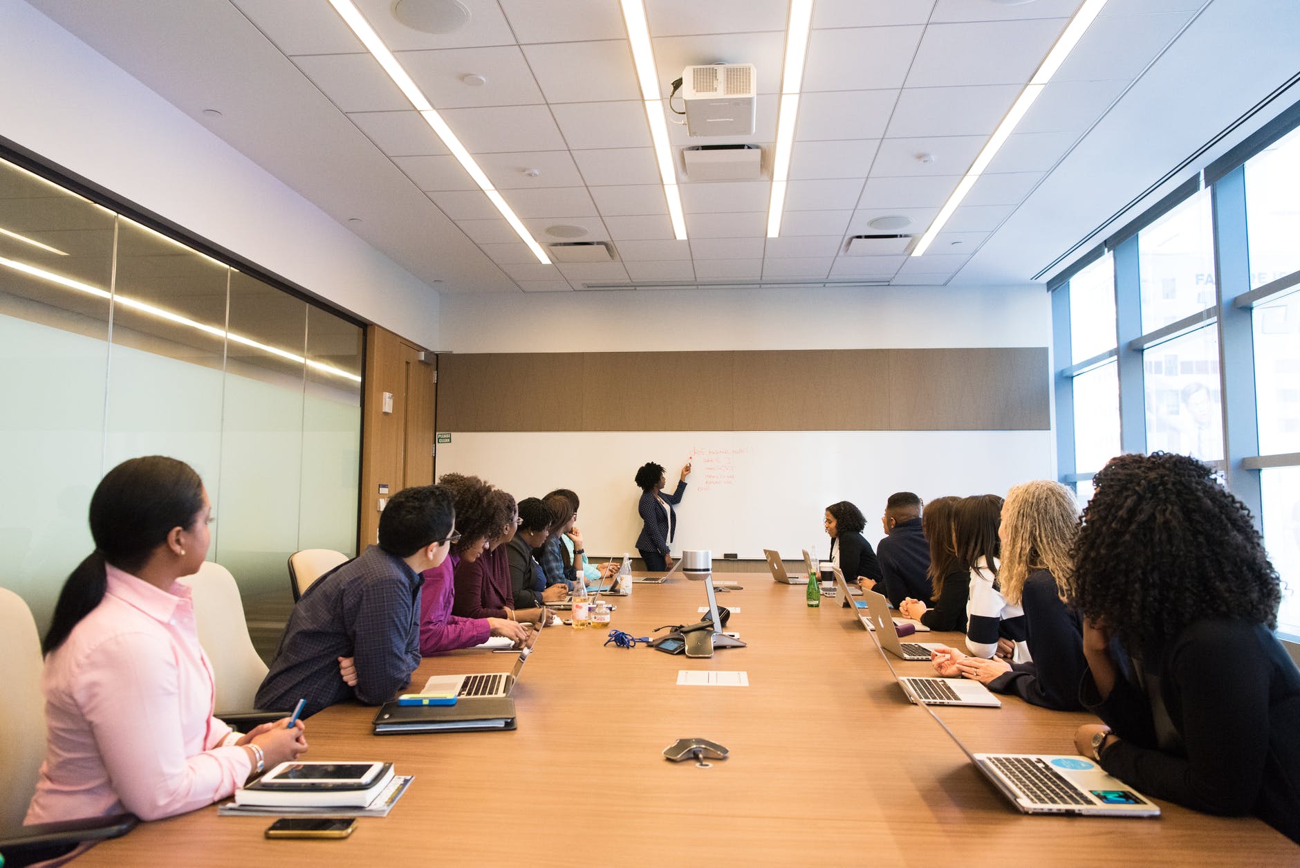 A conference room with a whiteboard and a group of people with laptops listening to a leader talking about Change Toxic Company Culture